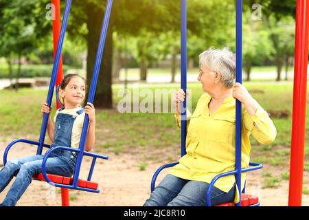 Das kleine Mädchen und ihre Großmutter spielen auf Schaukeln im Park Stockfoto