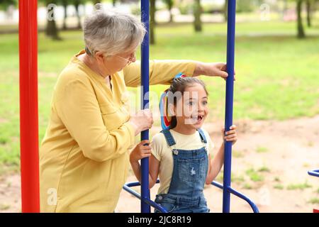 Kleines Mädchen mit ihrer Großmutter, die auf Schaukeln im Park spielt Stockfoto