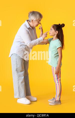 Das kleine Mädchen und ihre Oma berühren sich gegenseitig auf gelbem Hintergrund die Nasen Stockfoto