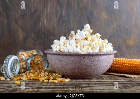 Eine große Schüssel mit Popcorn, Maiskörnern und Maiskolben auf einem Holztisch. Nahaufnahme. Stockfoto