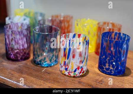 Set von mehrfarbigen Gläsern in verschiedenen Farben und Mustern, die auf einem Holzregal ruhen. Stockfoto