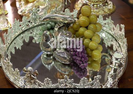 Verschiedene Obstsorten wie Äpfel, Birnen und Trauben in Silber und Keramik, die auf einer verspiegelten Silberschale ruhen. Stockfoto