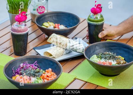 Mann Hand Nehmen Sie einen Pappbecher mit veganem grünen Smoothie in trendigen Outdoor-Café Stockfoto