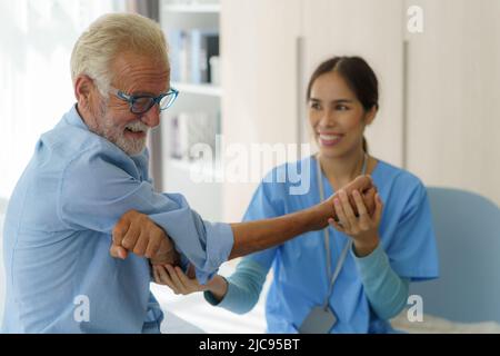 Leitender Mann Physiotherapie Übungen mit asiatischen Frau Betreuer oder Krankenschwester Physiotherapeut in Uniform hilft älteren männlichen Patienten zu Hause. Stockfoto