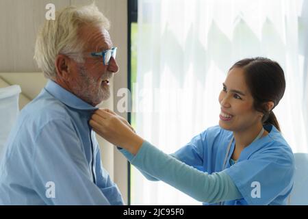 Junge asiatische Frau Krankenschwester helfen, Kleid zu behinderten älteren Mann im Bett im Altersheim. Tausendjährige Pflegekraft zur Unterstützung behinderter älterer Patienten Stockfoto