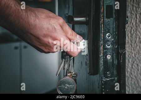 Die Hand öffnet das Schloss in der Tür mit einem Schlüssel Stockfoto