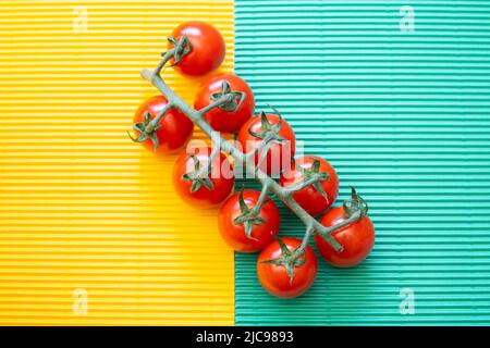 Neun Weinkirschtomaten auf welligem grünem und gelbem Hintergrund, Farbkontrast, von oben gesehen, Zenitansicht, horizontal Stockfoto