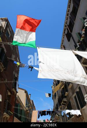 DIE ITALIENISCHE Flagge und die Kleidung hingen an sonnigen Tagen zwischen den Häusern der Stadt zum Trocknen auf Stockfoto