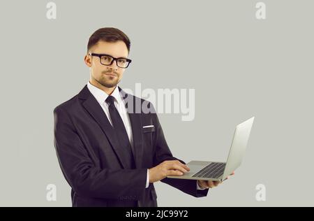 Porträt eines jungen selbstbewussten Geschäftsmannes mit Laptop in Händen isoliert auf grauem Hintergrund. Stockfoto