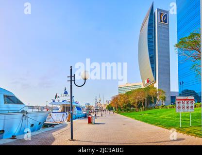 DUBAI, VAE - 1. MÄRZ 2020: Spazieren Sie entlang der Promenade des Creek im Viertel Port Saeed mit Blick auf das moderne Gebäude der Nationalbank und festverankerte Yachten, Stockfoto