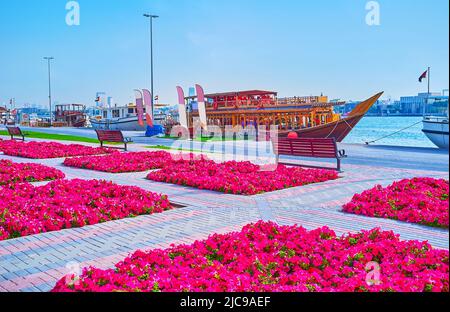 Die hellen Stiefmütterchen des Creek Side Park am Ufer des Dubai Creek mit Blick auf Boote und Daus, die am Ufer, Port Saeed, Rigga Al Buteen, Duba festgemacht sind Stockfoto