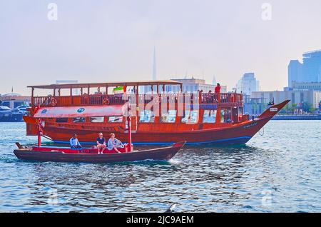 DUBAI, VAE - 1. MÄRZ 2020: Traditionelles hölzernes kleines Abra-Boot und großes Dhau-Boot auf dem Dubai Creek mit Silhouette des Burj Khalifa im Hintergrund Stockfoto