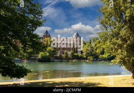 Turin, Piemont, Italien: Der Fluss Po mit dem Schloss Valentino (Castello del Valentino) zwischen den Bäumen im Park am Fluss und mit blauem Himmel und Stockfoto