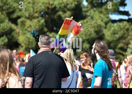 Menschen treffen sich am Startpunkt der Portsmouth Pride 2022 Parade. Helle Regenbogenfarben in der einen oder anderen Form sorgen für einen bunten Tag. Stockfoto