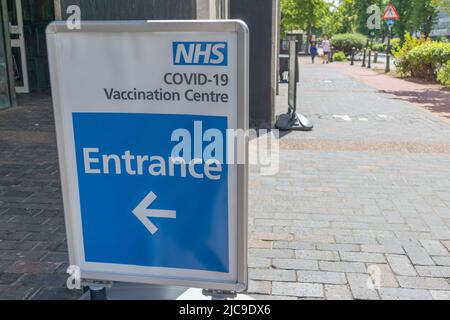 Southend on Sea, Großbritannien. Juni 2022. Ein Richtungsschild für ein NHS-COVID-19-Impfzentrum auf einem gemauerten Bürgersteig in einem städtischen Gebiet des Vereinigten Königreichs. Das Schild zeigt den Eingang mit einem nach links zeigenden Pfeil an. Fußgänger und ein Kreuzungsschild sind im Hintergrund sichtbar, was die Infrastruktur für das öffentliche Gesundheitswesen während der Pandemie hervorhebt. Ein Spaziergang im COVID 19-Impfzentrum in Southend. Penelope Barritt/Alamy Live News Stockfoto