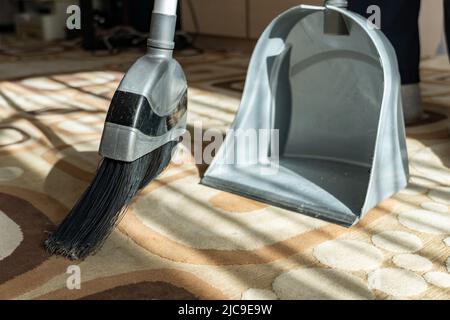 Wischen Sie den Staub mit einer Bürste vom Boden. Staub steigt in die Luft. Wischen Sie den Schmutz in einer Kehrschaufel vom Teppich. Reinigen Sie das Haus. Reinigen. C Stockfoto