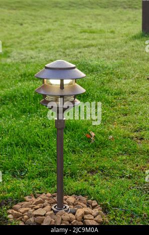 Gartenlaterne, umgeben von Steinen auf einem Hintergrund von hellgrünem, üppigem Gras Stockfoto