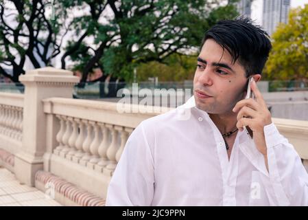 Stilvoller junger Latino-Mann, der die Straße entlang läuft, während er am Handy telefoniert. Stockfoto
