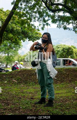 Medellin, Antioquia, Kolumbien - Februar 19 2022: Kolumbianerin mit langen braunen Haaren hält ihre Kamera in einem schönen Garten nahe der Straße Stockfoto