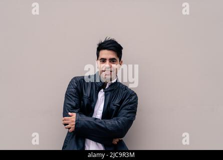 Halblanges Foto eines jungen Latinos, der sich an einer schlichten, farbigen Wand lehnt. Urbane Kleidung. Stockfoto