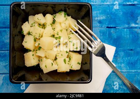 Kartoffel- und Petersiliensalat in einer schwarzen Schüssel auf einem rustikalen blauen Hintergrund. Stockfoto