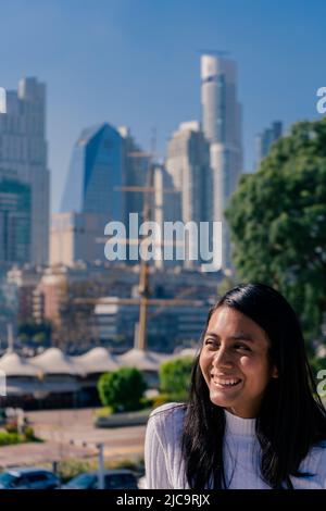 Mittellange Aufnahme einer lächelnden, schwarzhaarigen Latina-Frau mit der Stadt im Hintergrund. Stockfoto