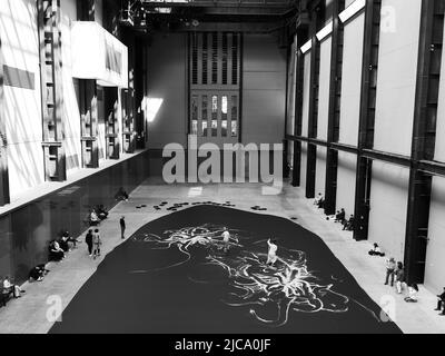 London, Großraum London, England, Juni 08 2022: Monochrom. Interieur der Tate Modern mit einer Live-Ausstellung, die von Besuchern beobachtet wird. Stockfoto