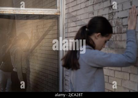 Das junge Paar spiegelte sich durch ein Glas. Junge, der neben einem traurigen Mädchen steht. Paar im Konflikt. Stockfoto