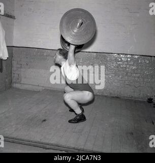 1957, historisch, Gewichtheben, in einer Turnhalle auf einem Holzbrett, ein männlicher Gewichtheber trainiert, beim Schnappen, Stockport, England, Großbritannien. Die Schlinge ist eine der beiden Lifte im Wettkampftraining oder im olympischen Gewichtheben. Er trägt Gewichtheben, aber nicht den traditionellen breiten Gewichtheben-Gürtel aus Leder. Stockfoto