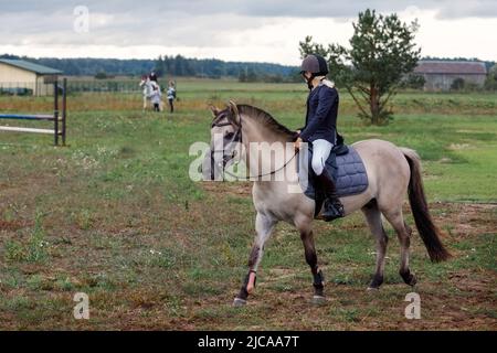 Schulungsprozess. Junge Teenager-Mädchen Reiten Trabrennen graues Pferd auf Gras Arena üben in der Reitschule. Farbe im Freien horizontale Sommerzeit Stockfoto