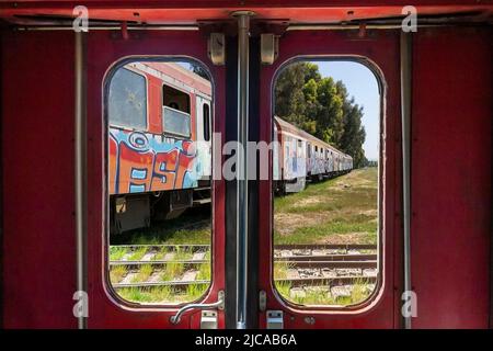 Verlassener Zug aus der kommunistischen Zeit durch das Fenster an der Tür eines anderen alten Zuges in Durres, Albanien Stockfoto