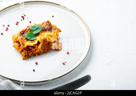 Italienische Lasagne mit Tomatenbolognesauce und Hackfleisch, auf Teller, auf weißem Steinhintergrund, mit Kopierraum für Text Stockfoto