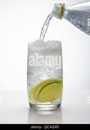 Wasser gießt in ein Glas Eis und Zitronenscheiben auf weißem Hintergrund Stockfoto