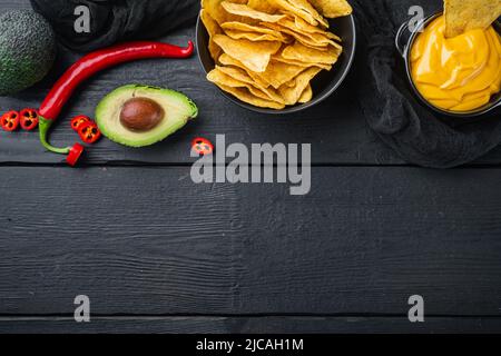 Dreieckiger gelber Maistortilla-Chip mit Soße, auf schwarzem Holzhintergrund, Draufsicht oder flacher Lay mit Kopierraum für Text Stockfoto