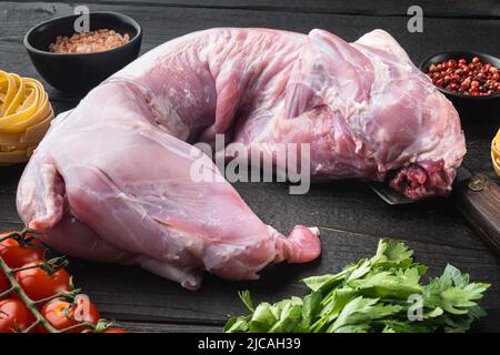 Ganzes Kaninchen, rohes Fleisch mit Gewürzen und Gemüse für Tagliatelle-Eintopf, auf schwarzem Holztischhintergrund Stockfoto