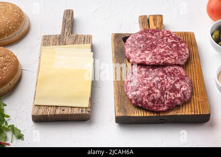 Zutaten zum Kochen von Burgern. Roh gemahlenes Rindfleischschnitzel, auf weißem Steinhintergrund Stockfoto