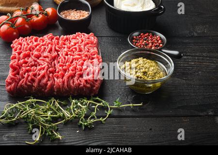 Rohe Fleischbällchen aus gemahlenen Rindfleischzutaten, auf schwarzem Holztischhintergrund Stockfoto