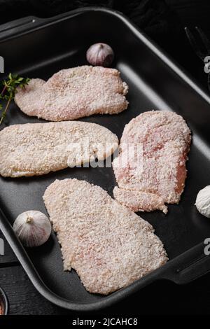 Hausgemachtes, roh paniertes deutsches Weiner Schnitzel-Set, auf schwarzem Holztischhintergrund Stockfoto