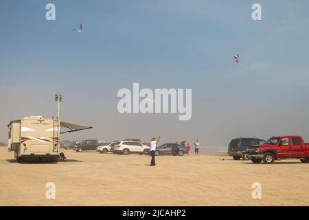 PORT ARANAS, TX - 16. FEB 2020: Autos und andere Fahrzeuge und Menschen, die an einem windigen Tag Drachen an einem verschwommenen und sandigen Strand fliegen. Stockfoto