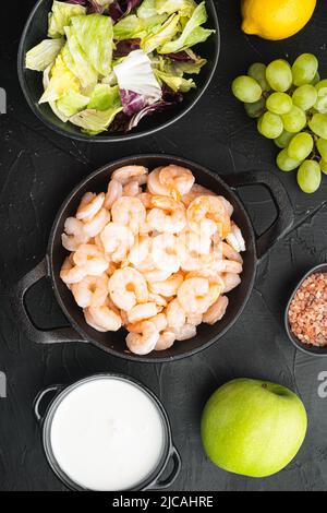Frische Sommer-Vitaminvorspeise aus grünem Salat, Garnelen, Oliven Zutaten, mit Soße Apfel und Traube, auf schwarzem Stein Hintergrund, Blick von oben flach gelegen Stockfoto