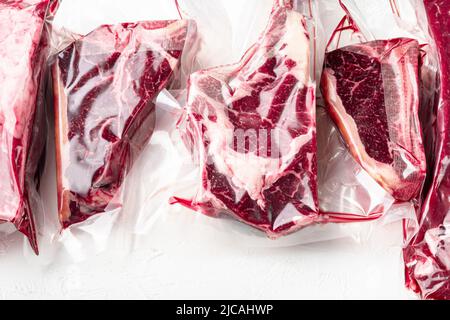 Rohes Rindfleisch in der gesaugten Hautpackung, Tomahawk, t Bone, Clubsteak, Rib Eye und Filet, auf weißem Steinhintergrund Stockfoto