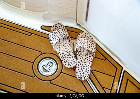 Sandalen mit Lepardendruck auf der Yacht mit synthetischem Teak-Boot-Deck - Nahaufnahme mit Reflexen an der Seite des Bootes. Stockfoto