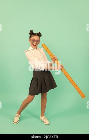 Glückliches Kind in Schuluniform und Brille mit Mathe-Lineal auf blauem Hintergrund, Kindheit Stockfoto