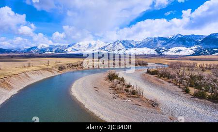 Fluss schlängelt sich um frühe Winterfelder mit schneebedeckten Bergen im Hintergrund Stockfoto