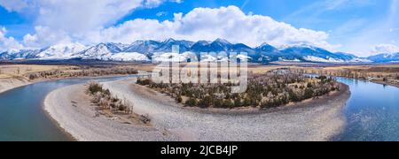 Panorama des Flusses, der sich um den Frühlingswald dreht, mit atemberaubenden schneebedeckten Bergen am Horizont Stockfoto