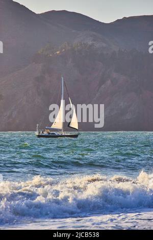 Segelboot beim Navigieren auf den Wellen des Ozeans durch die Berge Stockfoto