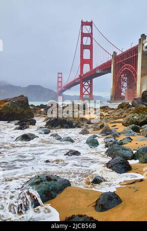 Meereswellen krachen am nebligen Morgen am Sandstrand der Golden Gate Bridge Stockfoto