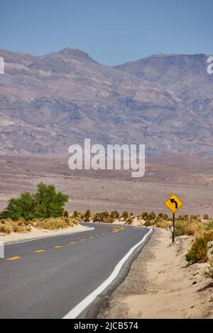 Asphaltierte Straße in Wüstenlandschaft, die zu scharfen Wendung und Bergen führt Stockfoto