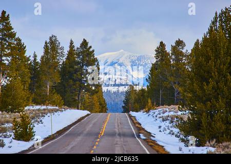 Straße im Winterschnee, die zu atemberaubenden Berggipfeln führt Stockfoto