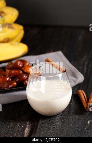 Banane, Datteln Obst und Zimt Smoothie oder Milchshake in einem Glas auf einem Holztisch mit grauem Hintergrund, ausgewählter Fokus Stockfoto